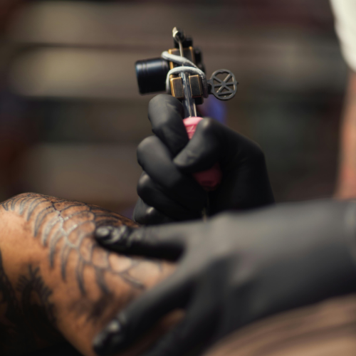 Machine à tatouer tenue par une main gantée au-dessus d’un tatouage coloré dans un salon de tatouage  dans Lanaudière